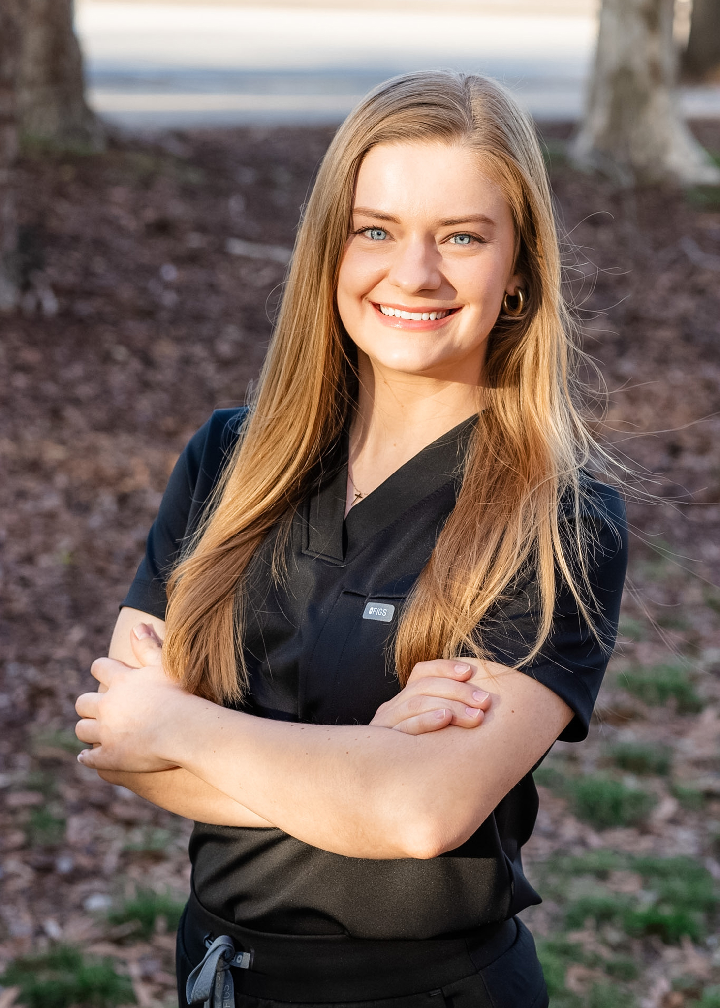 Smiling woman in medical attire outdoors.