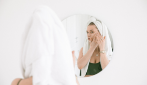 A woman examining her face in a bathroom mirror for skin changes before scheduling a skin cancer screening in Chattanooga.