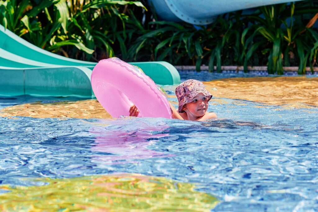 Child swimming in chlorinated pool water during summer with sun hat and float