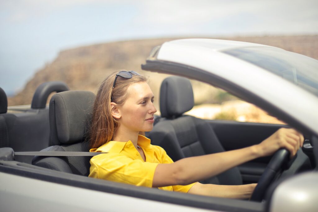 Woman driving in summer sun with exposed skin showing risk of UV damage from sunscreen application mistakes
