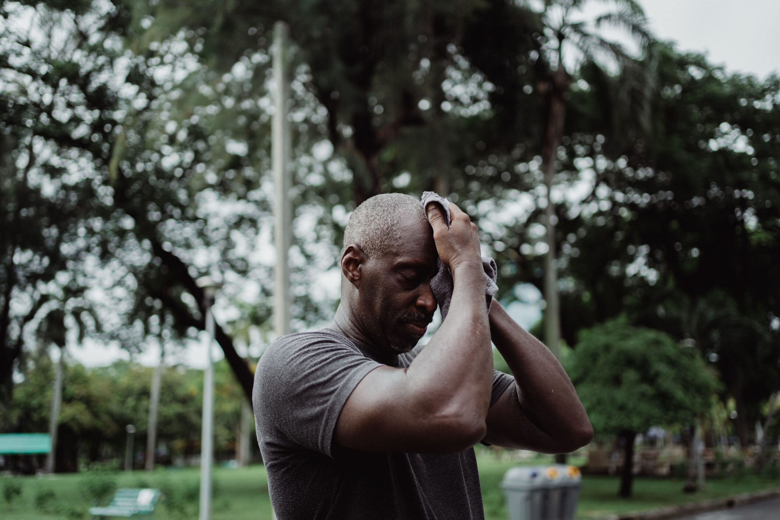 Man wiping sweat from his face while exercising outdoors in warm weather