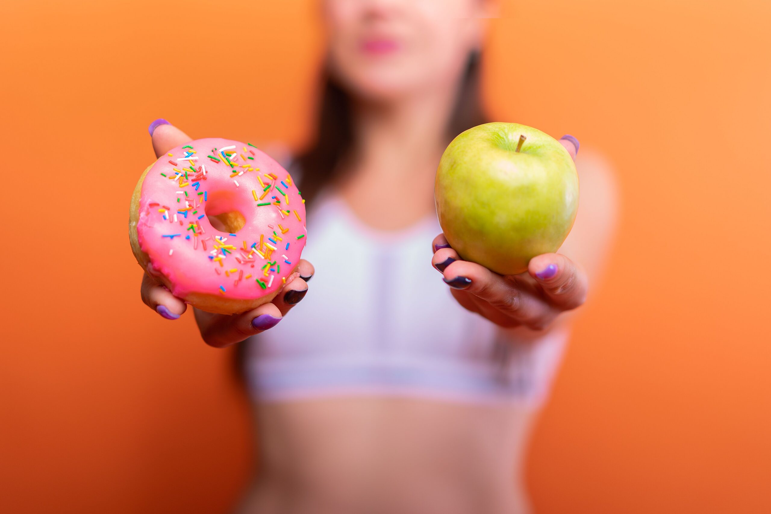 Woman choosing between a donut and an apple representing nutritional deficiencies that cause hair loss