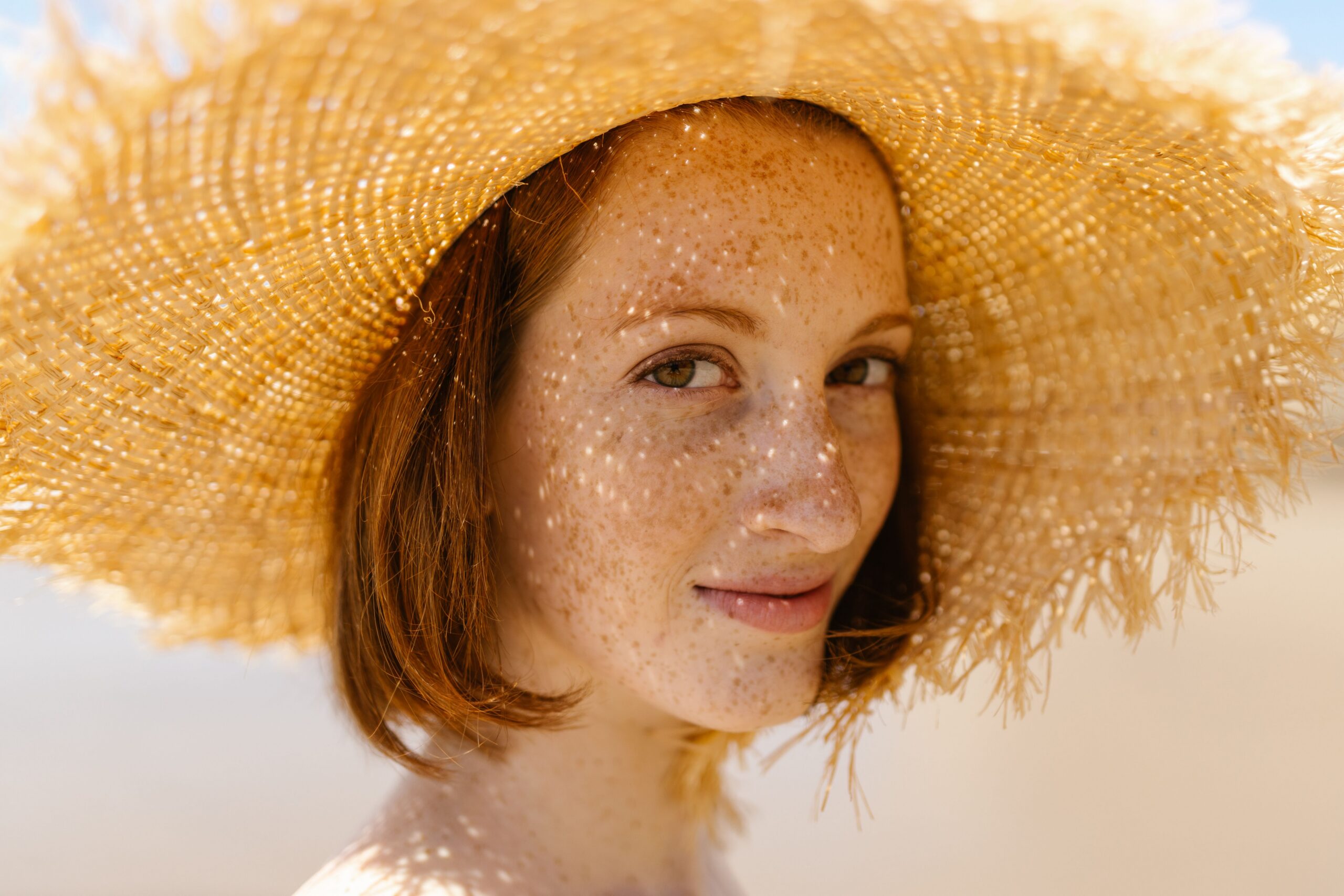 Fair skinned woman with freckles and red hair wearing a sun hat to protect against skin cancer risk